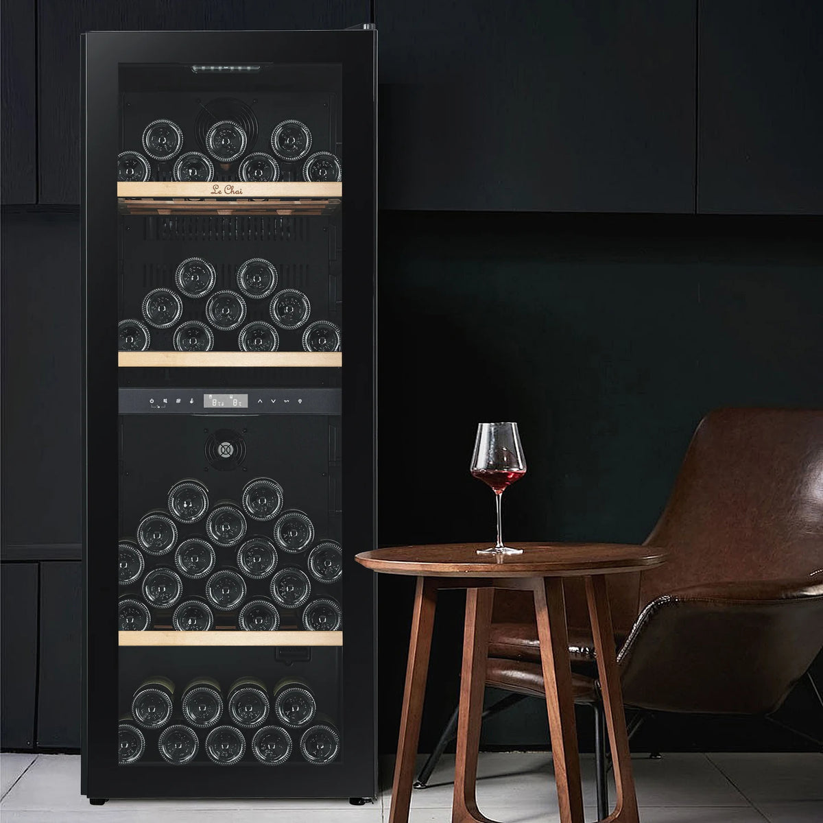 Cave de vinho Le Chai LCT2FS100 de 100 garrafas, numa sala de estar junto a uma mesa com um copo de vinho tinto, com as prateleiras de madeira sem frontal.